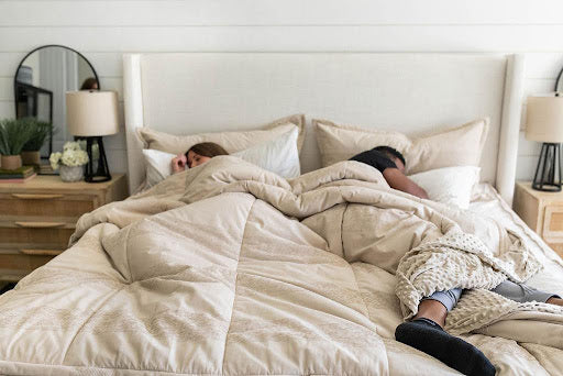 
      A man and woman asleep in. a bed with gray Bed-dys bedding and a neutral bed frame.
    