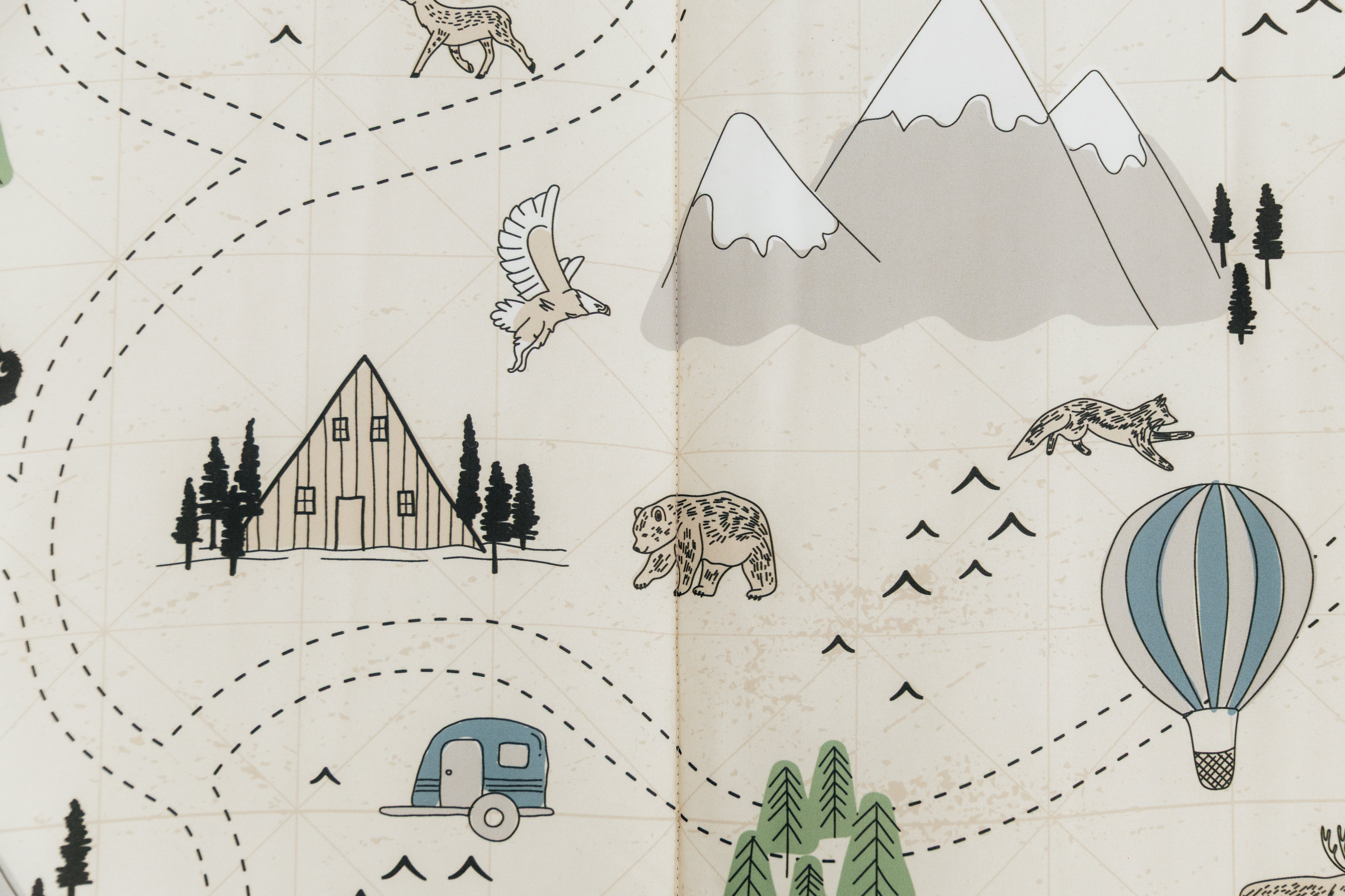 A close up on the print of an outdoor themed zipper bedding set, featuring animals, hot air balloons, mountains, cabins, and trees.