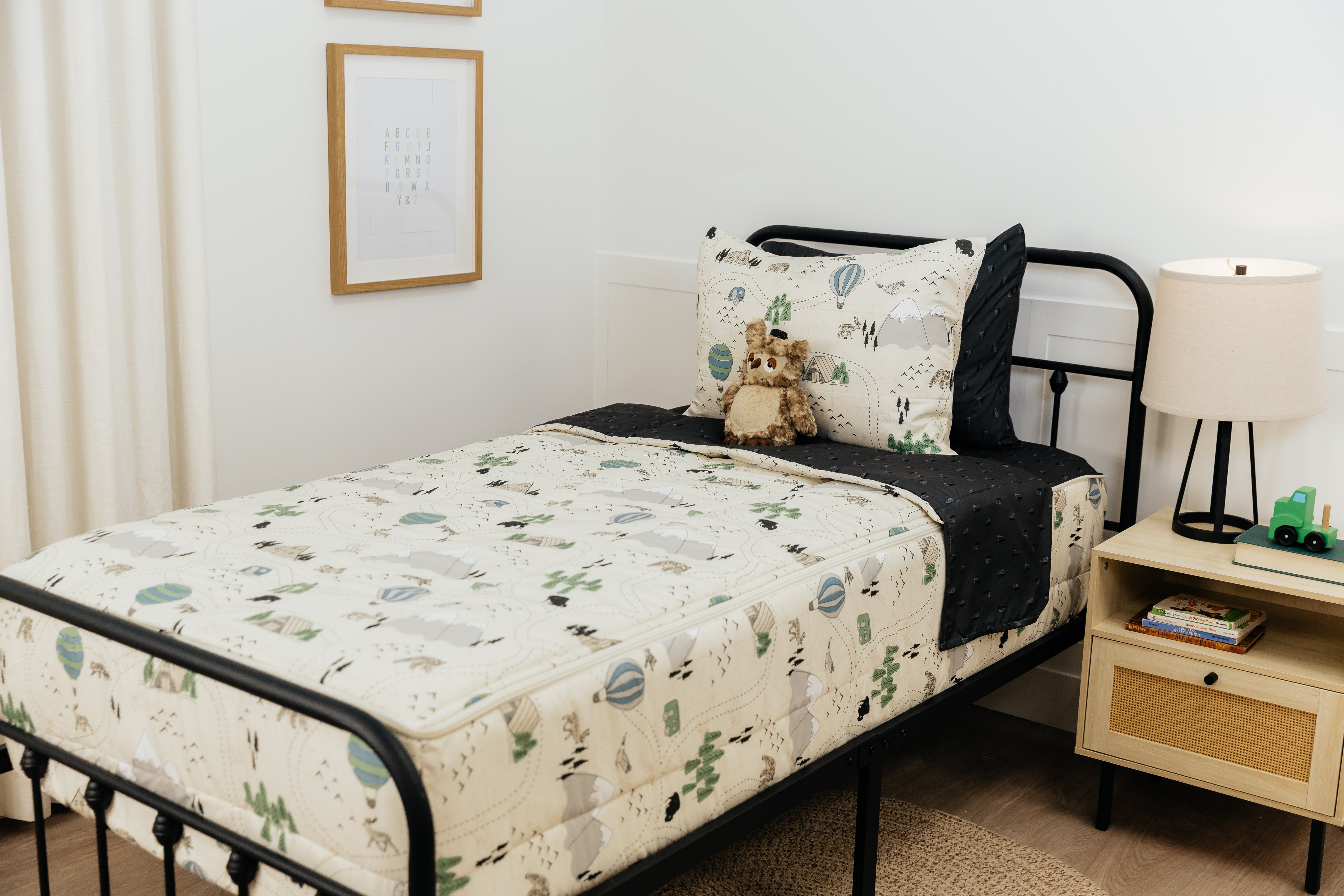 A twin bed made with outdoor themed zipper bedding, a stuffed owl propped up against the pillows.
