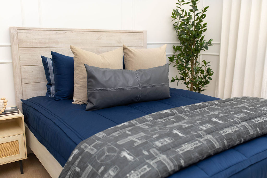 A bed made with navy blue zipper bedding and an assortment of neutral and striped throw pillows and blanket.