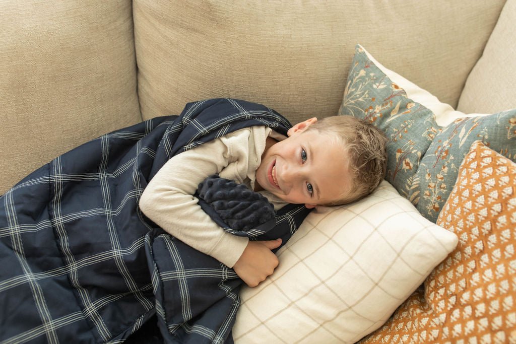 A child smiling on couch cuddling with a navy blue plaid pattern children's blanket.