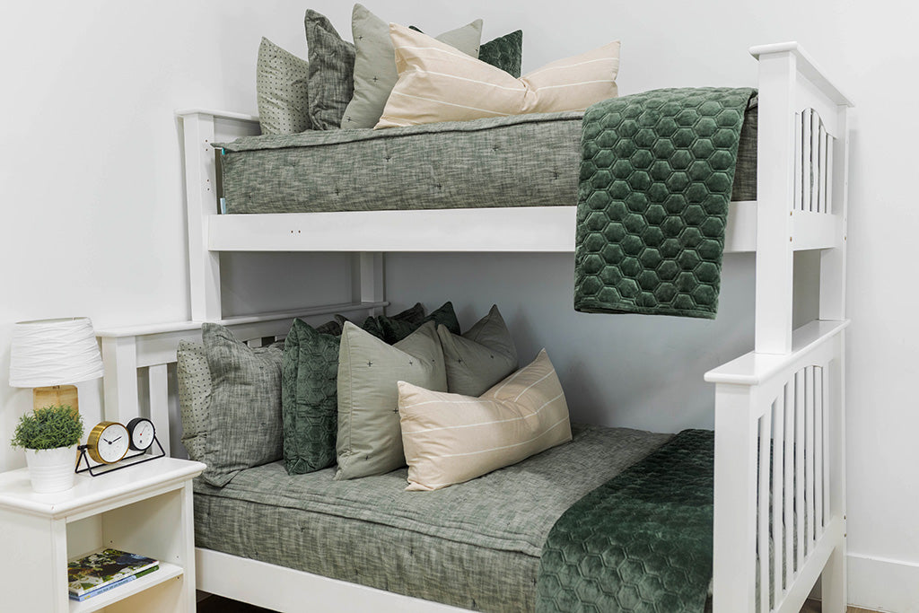 A standard bunk bed with both bunks made with deep emerald green zipper bedding and neutral and green velvet pillows and blankets.
